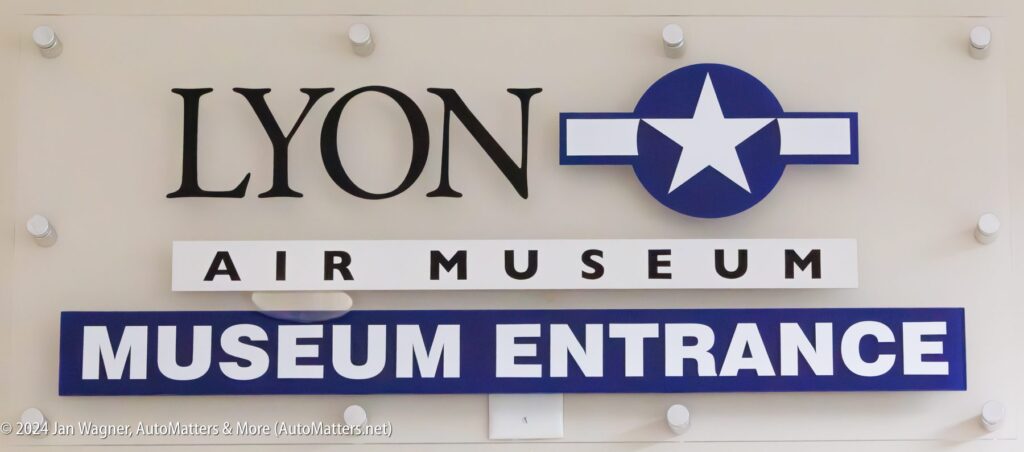 Sign for Lyon Air Museum with a blue and white star logo and bold text reading "MUSEUM ENTRANCE.