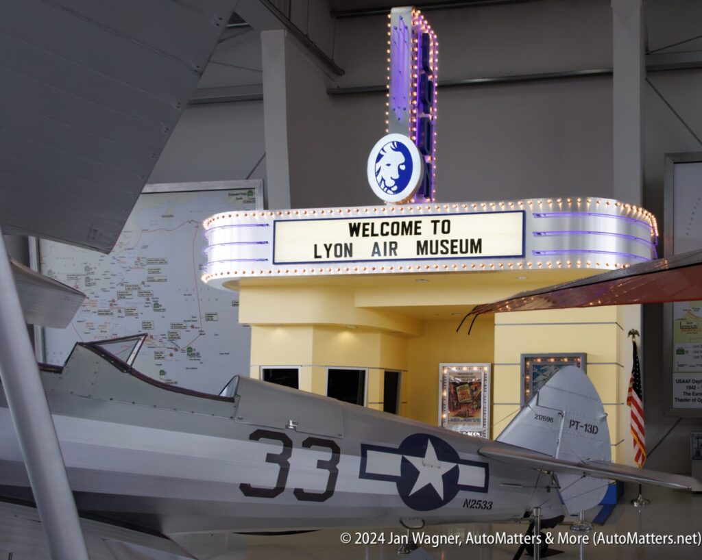 Entrance to Lyon Air Museum with vintage-style marquee sign, aircraft on display in foreground, and a map on the wall in the background.