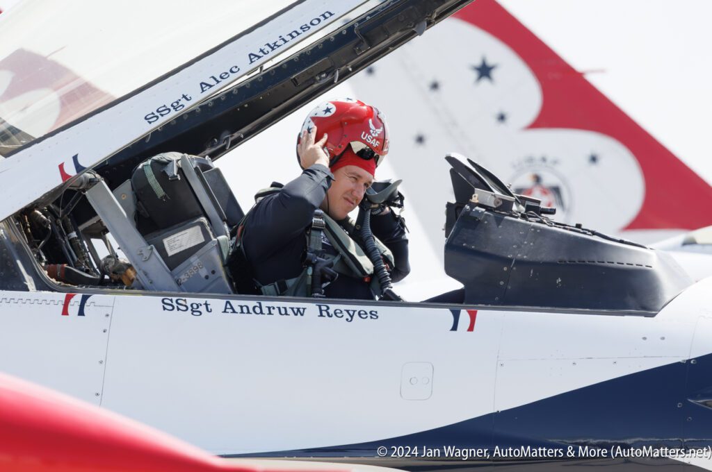 A pilot in uniform adjusts his helmet inside the cockpit of a jet labeled "SSgt Andruw Reyes," with another jet visible in the background.