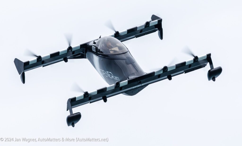 A black electric vertical takeoff and landing (eVTOL) aircraft with multiple rotors in flight against a white sky.