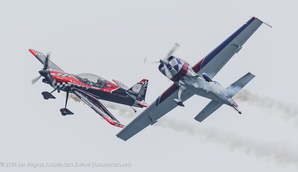 Two aerobatic airplanes perform close-proximity maneuvers in the sky, leaving smoke trails behind them during an airshow.