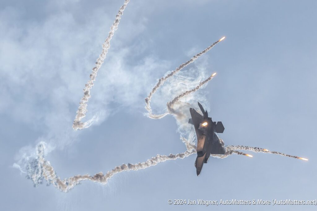 A fighter jet releases flares while maneuvering in the sky, leaving smoke trails behind it.