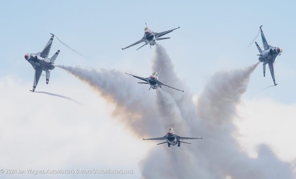 Four fighter jets perform an aerial maneuver, flying in formation with smoke trails against a cloudy sky.