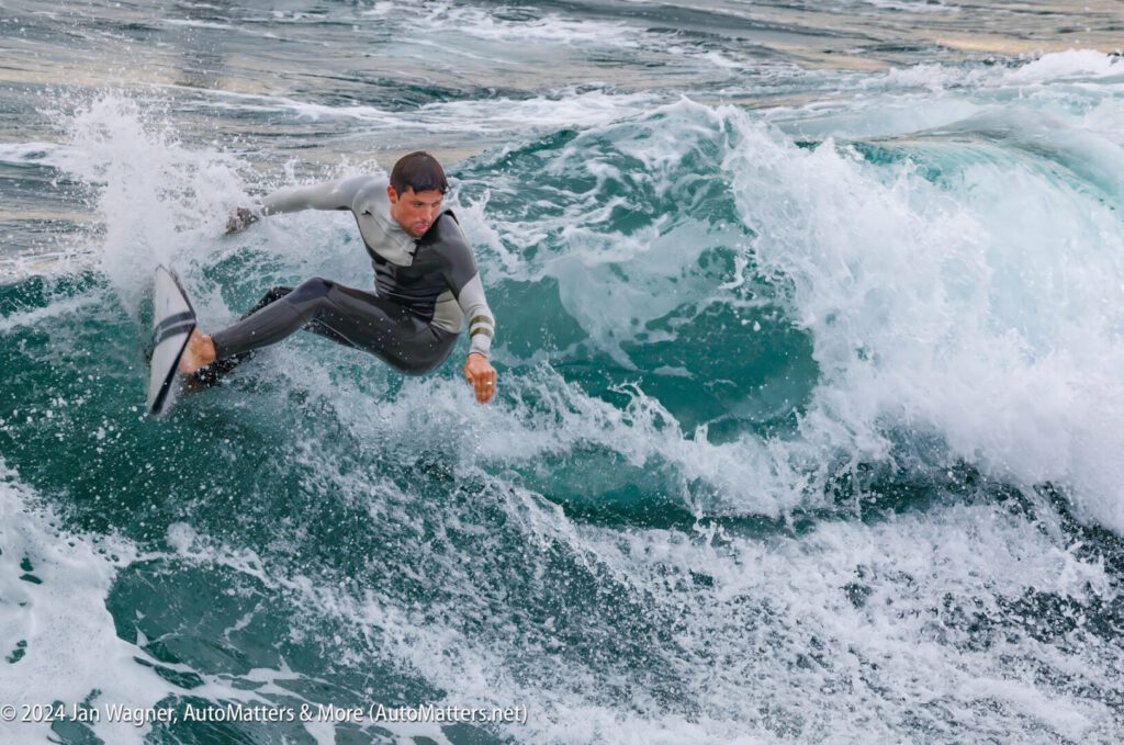 A person in a wetsuit rides a wave on a surfboard, turning sharply as water splashes around them.