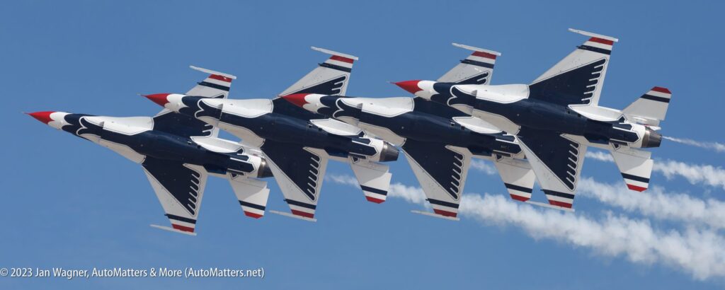 Six fighter jets with red, white, and blue paint fly in close formation against a clear blue sky, leaving white smoke trails behind them.