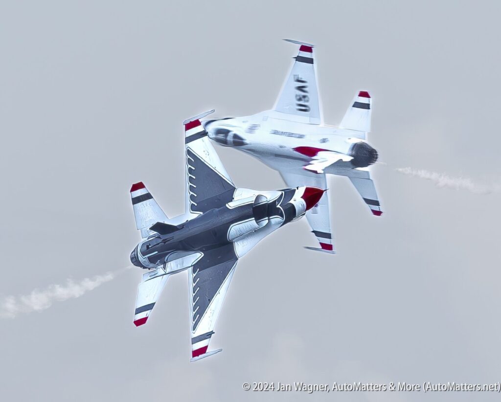 Two U.S. Air Force Thunderbirds jets fly past each other at close range during an air show, leaving smoke trails against a cloudy sky.