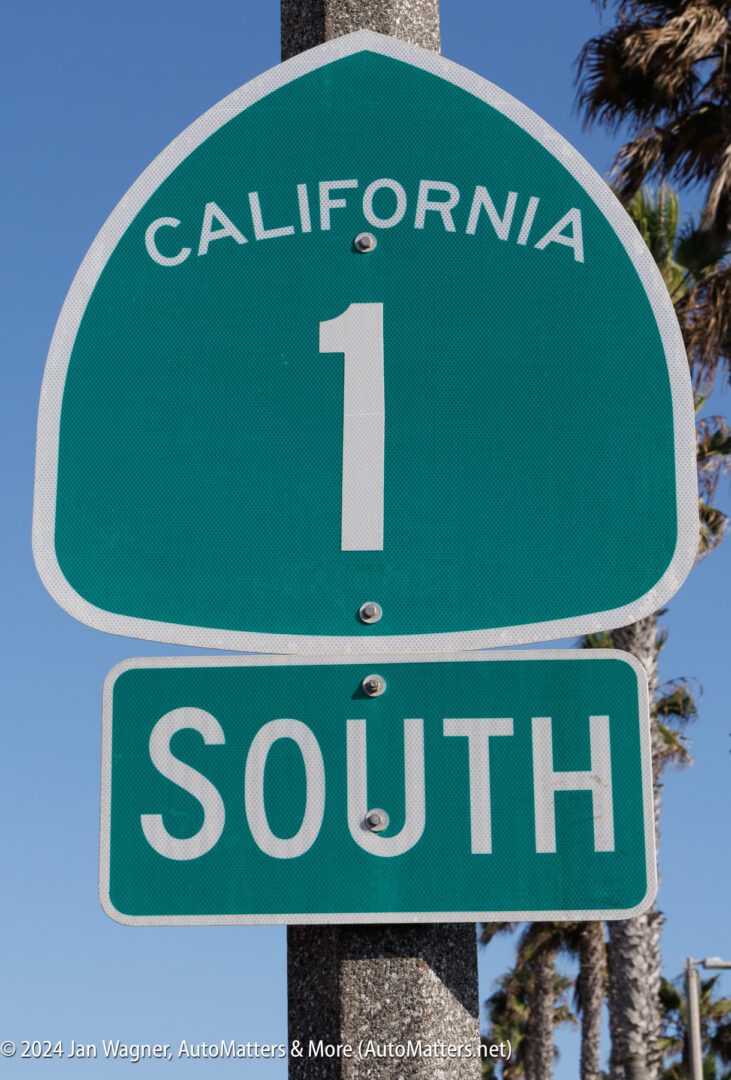 Green road sign for California State Route 1 indicating the southbound direction, with palm trees and blue sky in the background.