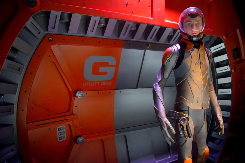 A man in a space suit standing in front of a red door.
