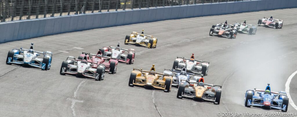 A group of indy cars racing down a track.
