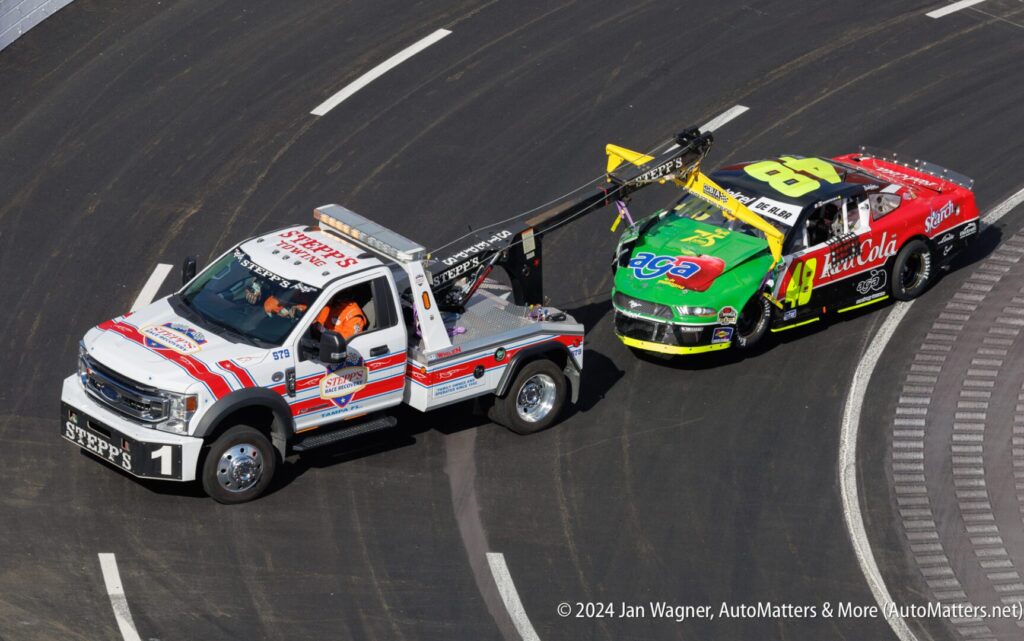 A tow truck towing a race car around a track.