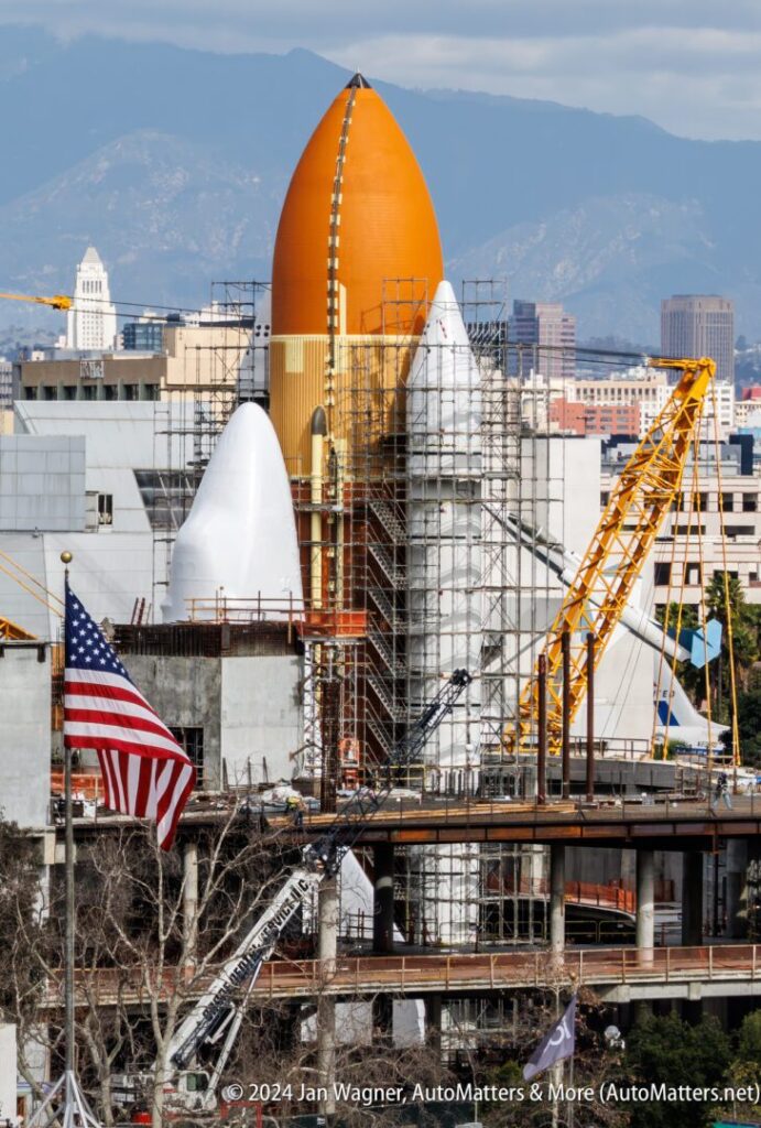 A large orange spaceship is under construction in a city.