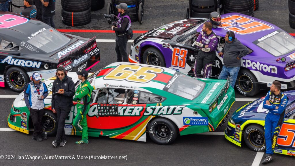 A group of nascar cars are lined up in a parking lot.