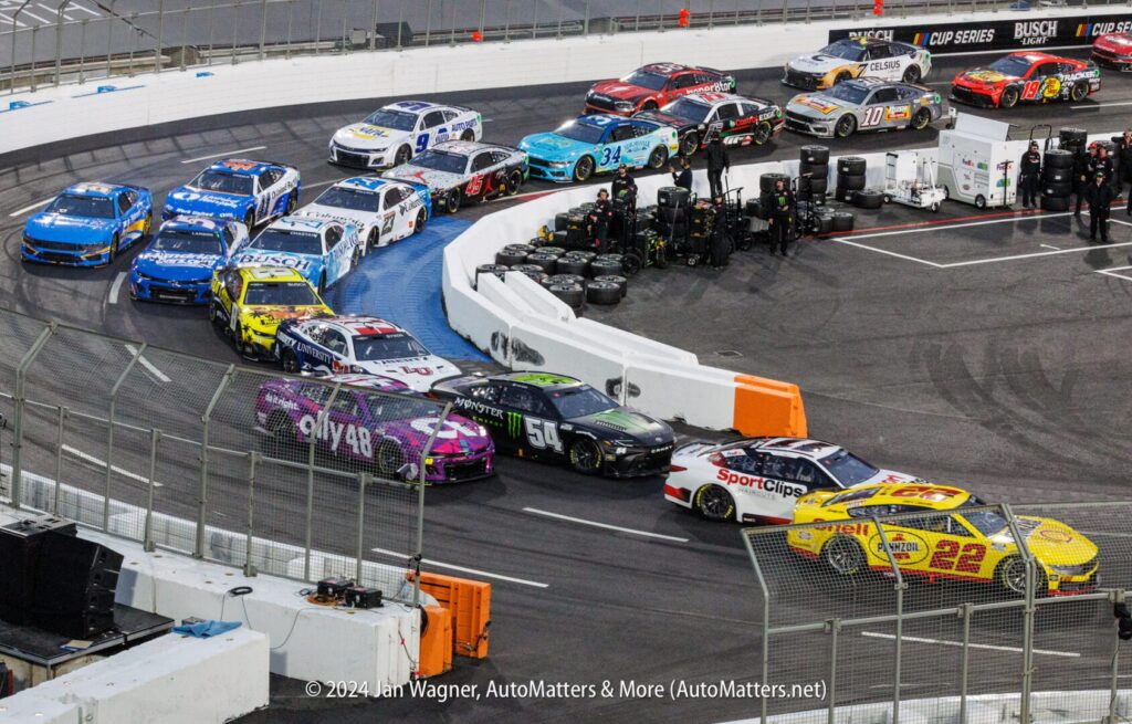 A nascar race with many cars on the track.