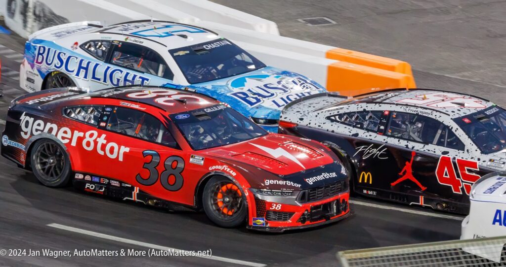 Three nascar cars are racing on a track.