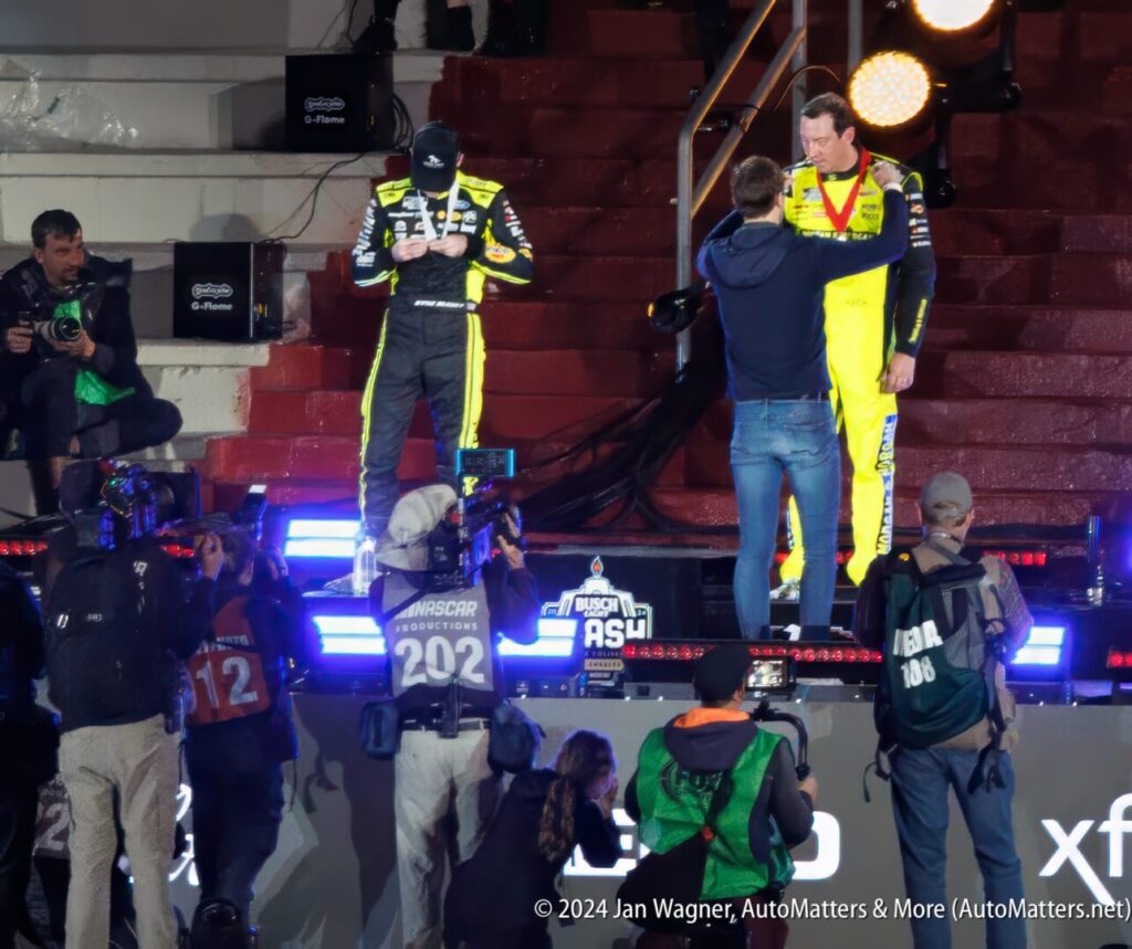 Two nascar drivers standing on a podium.