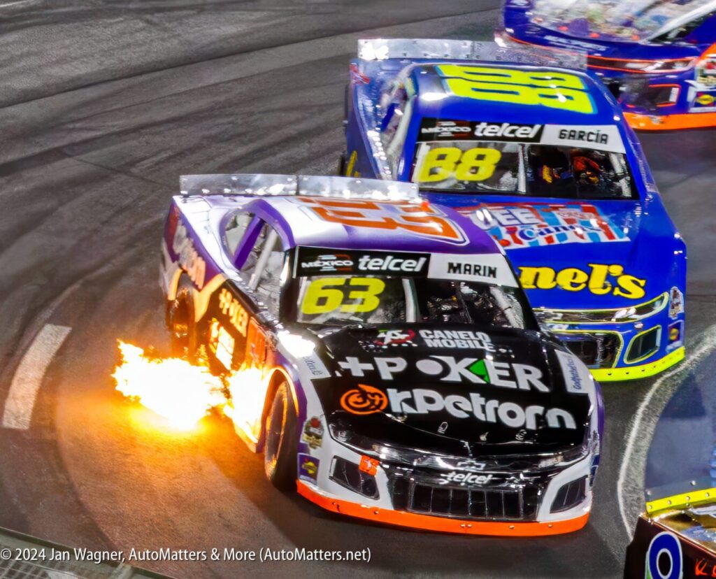 Three nascar cars racing on a track with flames.