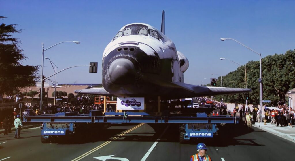 A space shuttle is being transported down the street.