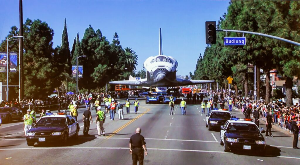 A space shuttle is parked on a street in front of a crowd of people.