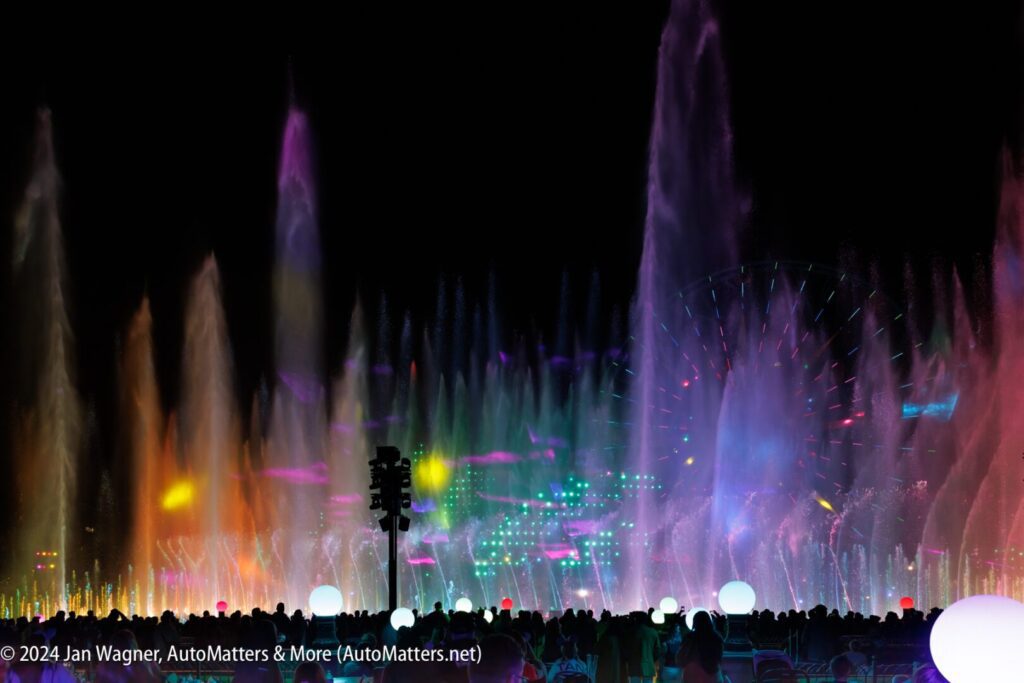 A large group of people standing in front of a colorful water fountain.