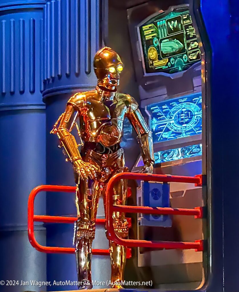 A golden c-3po standing in front of a monitor.