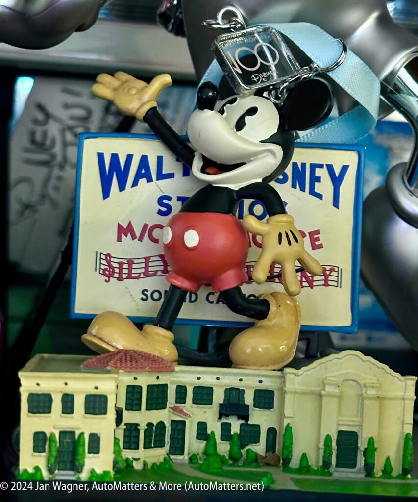 A mickey mouse figurine is standing next to a wall disney sign.