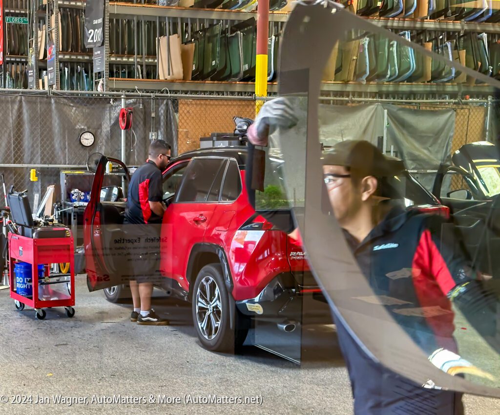 Workers in an auto glass repair shop replace the windshield of a red SUV.