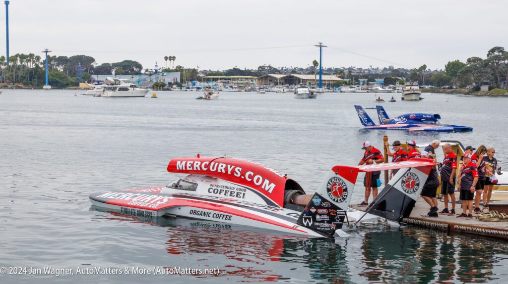 A hydroplane boat labeled "MERCURY'S" is docked in a marina with team members standing nearby; another hydroplane is visible in the water behind them.