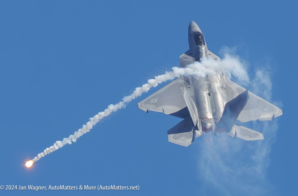 A fighter jet releases a flare while flying against a clear blue sky.