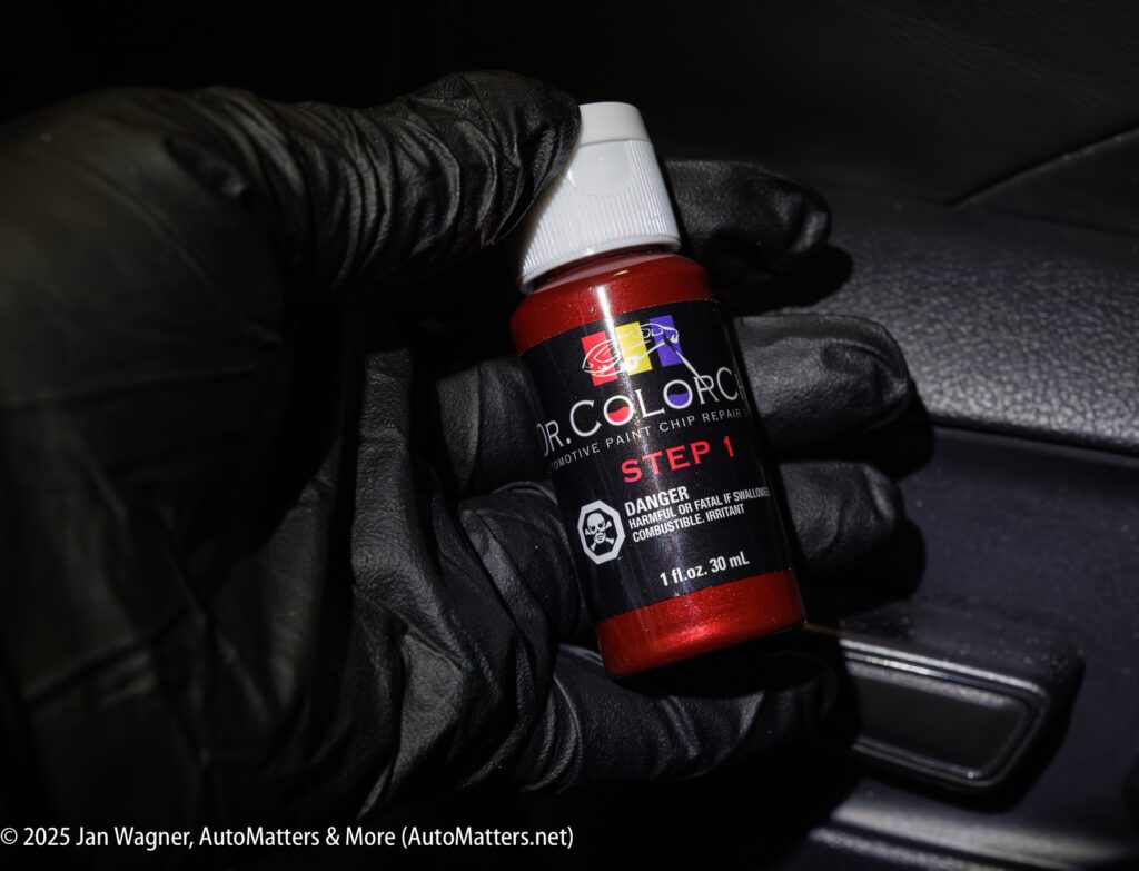 A gloved hand holds a small bottle labeled "Dr. ColorChip Step 1" with a warning for hazardous chemicals. The bottle is red and the image is taken inside a vehicle.