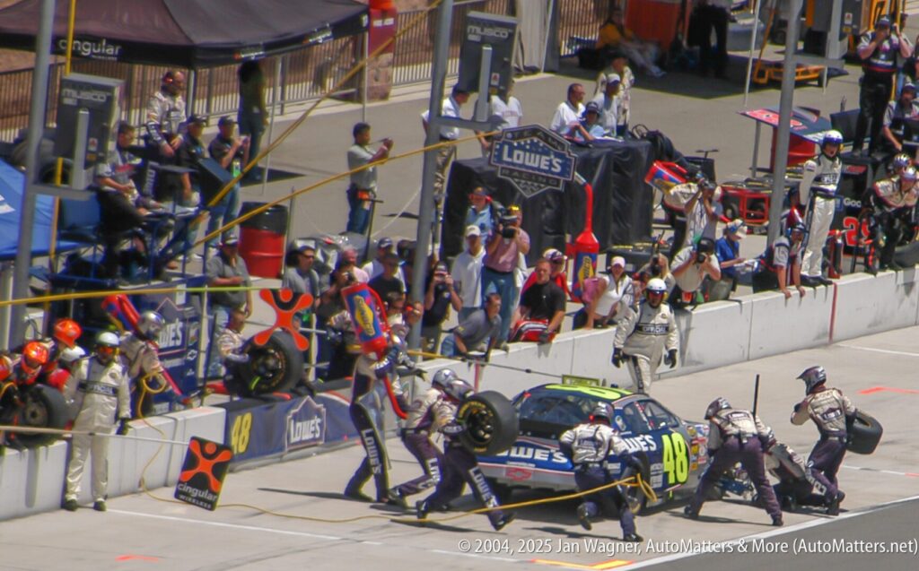 Pit crew services a #48 race car during a pit stop as spectators watch from behind barriers at a motorsport event.
