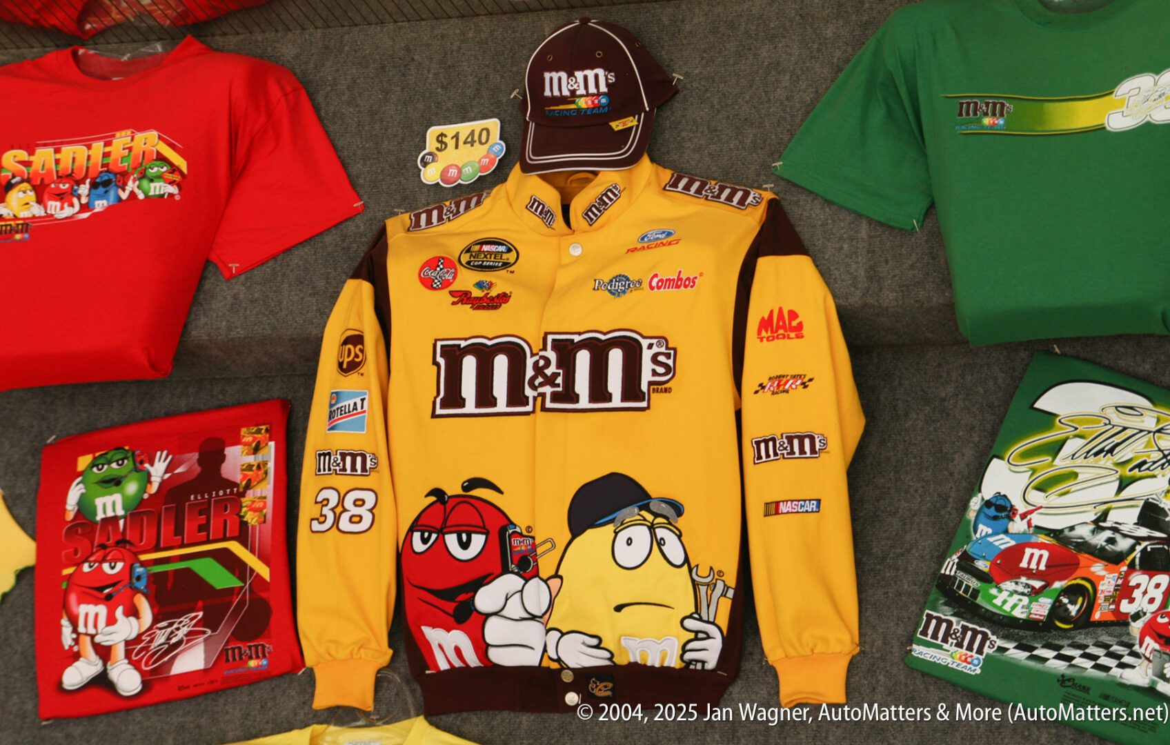 A yellow and brown M&M's racing jacket, matching cap, and T-shirts with M&M's characters and race car graphics displayed on a surface.