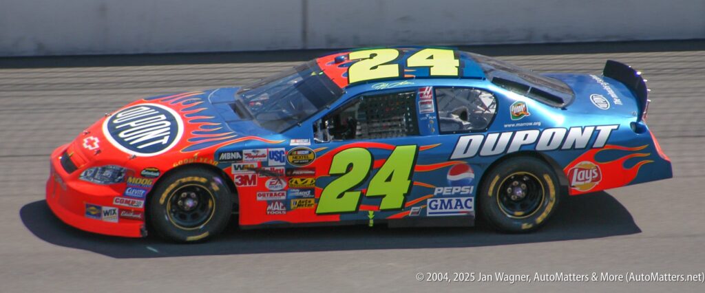 A blue and red NASCAR race car with the number 24 and "DuPont" branding drives on a racetrack.