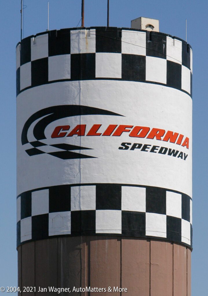 A water tower painted with a black-and-white checkered pattern displays the "California Speedway" logo against a clear blue sky.