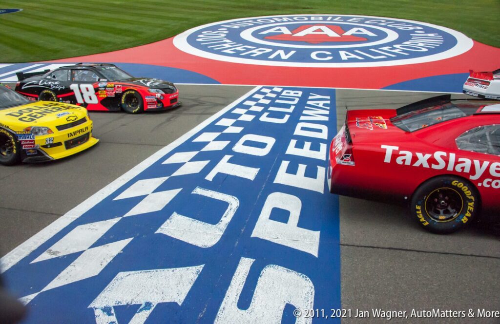 Three NASCAR race cars cross the finish line at Auto Club Speedway, with a large AAA Southern California logo visible in the background.