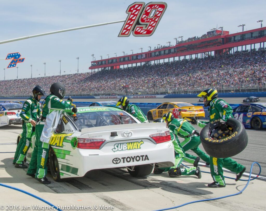 Pit crew services a white Toyota race car sponsored by Subway, with the number 19 visible above, during a NASCAR race at a crowded speedway.