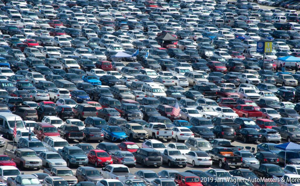 A large parking lot filled with tightly parked cars of various colors, viewed from above.