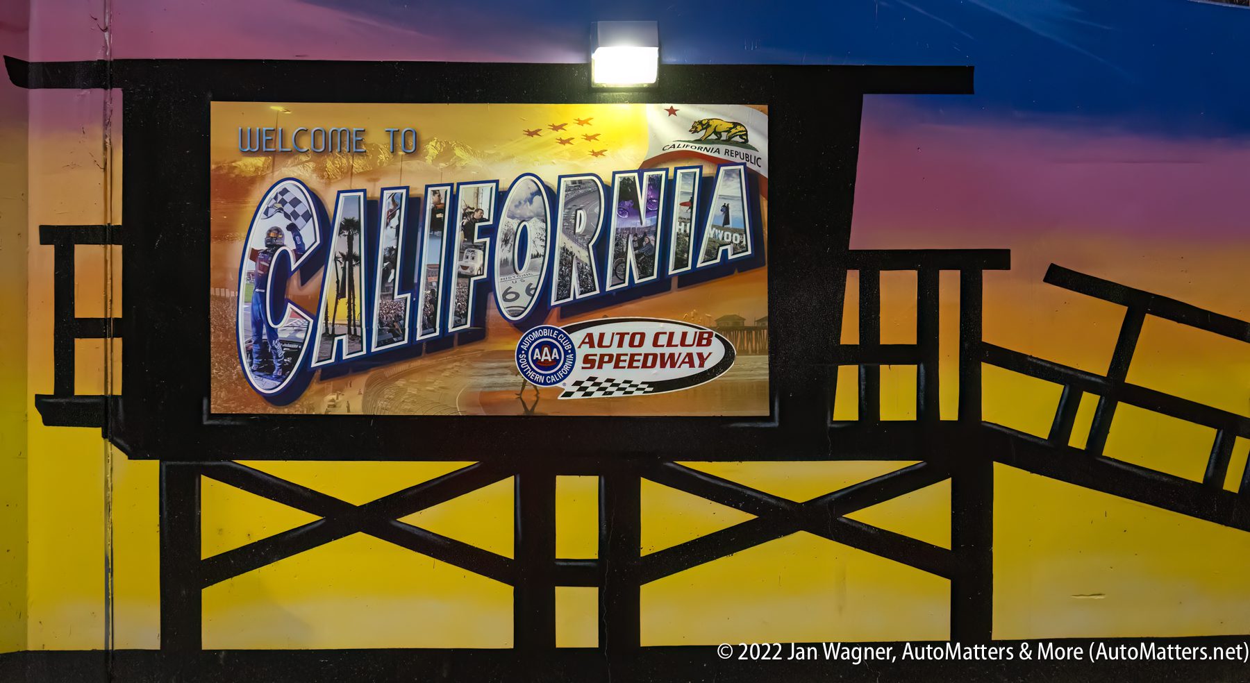 02036-20220226 NASCAR Xfinity Series Production Alliance Group 300 race-Sand barrel impact+Cup qualifying-Auto Club Speedway-Fontana CA_24-240mm-R3 A colorful mural displays "Welcome to California" and "Auto Club Speedway" with racing graphics, set against a sunset sky with a lifeguard tower silhouette.