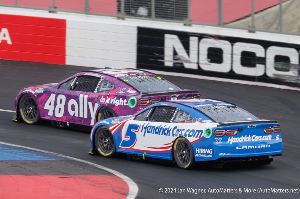 Two NASCAR race cars compete on a track; car 48 is purple with Ally branding, car 5 is blue with HendrickCars.com branding.