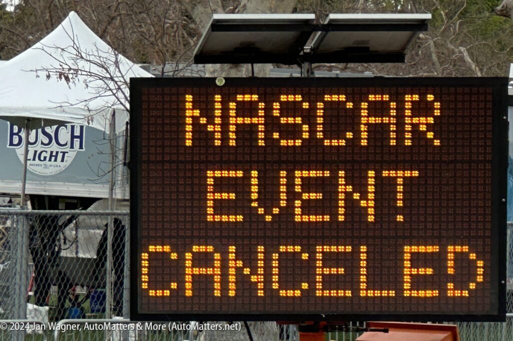 Electronic sign displays the message "NASCAR EVENT CANCELED" near a fence with a Busch Light tent visible in the background.