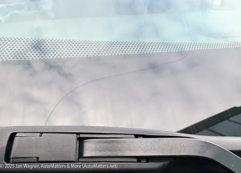 A windshield with a visible crack running across the glass, located near the bottom edge behind a windshield wiper.