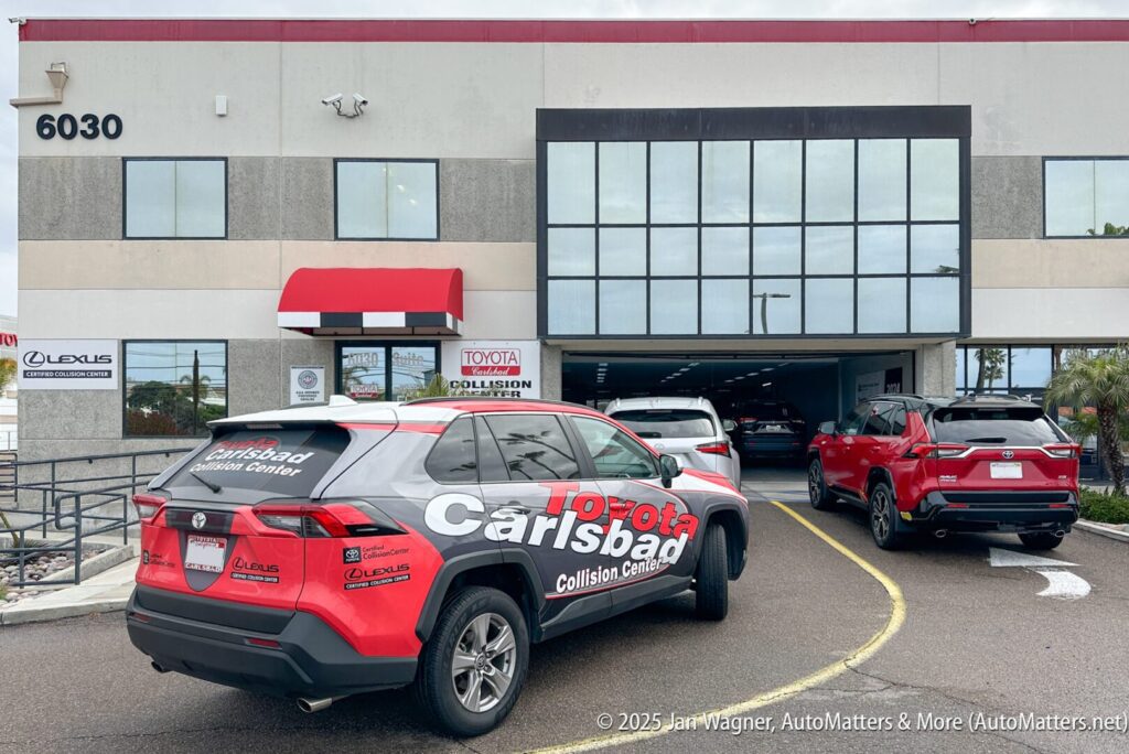 Several vehicles, including a Toyota Carlsbad Collision Center SUV, are parked outside and entering a service garage at a commercial auto repair facility.