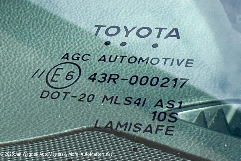 Close-up of a Toyota windshield marking showing manufacturer details, safety certifications, and codes including "AGC Automotive," "43R-000217," and "LAMISAFE.