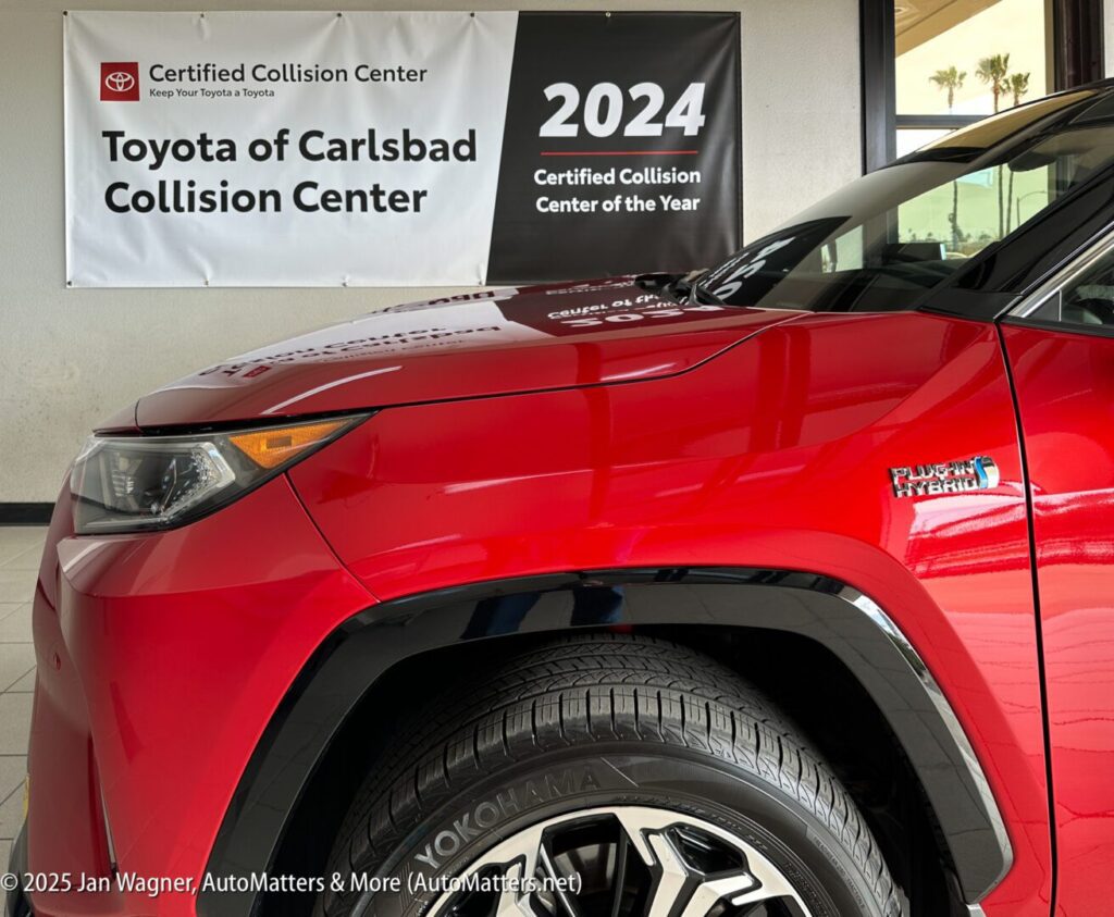 A red Toyota RAV4 Hybrid is parked in front of a banner reading "Toyota of Carlsbad Collision Center - 2024 Certified Collision Center of the Year.