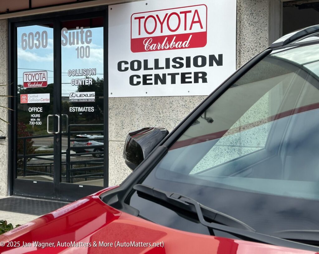Entrance of Toyota Carlsbad Collision Center showing signage, office hours, and part of a red car in the foreground.