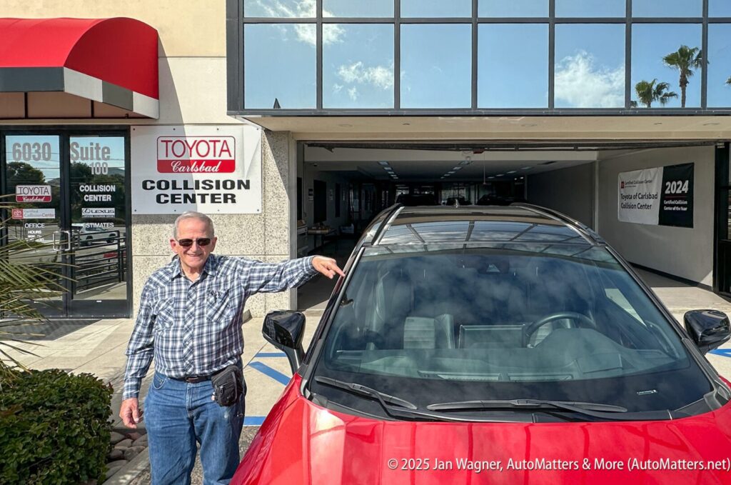 A man in sunglasses stands next to a red car outside a Toyota Carlsbad Collision Center building under a clear sky.