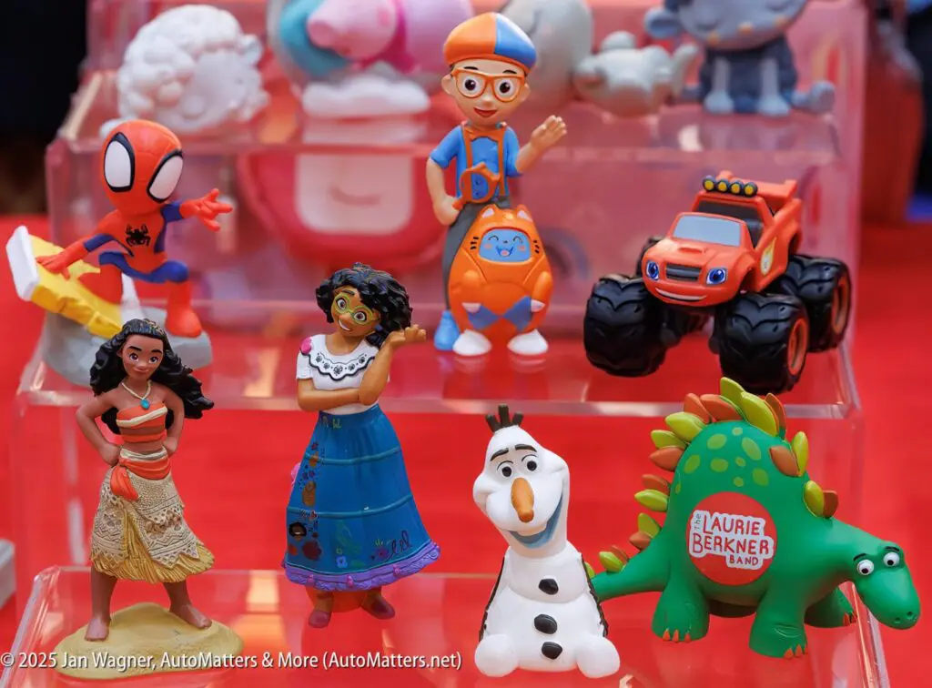 A display of colorful toy figurines, including characters resembling superheroes, animated movie figures, a monster truck, and a dinosaur, arranged on clear plastic tiers.