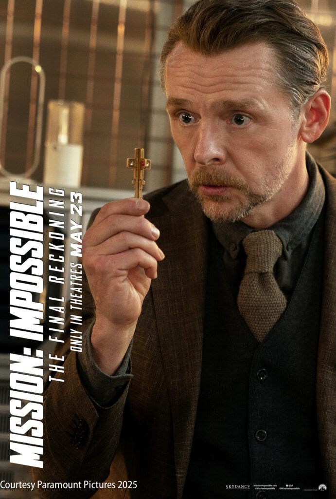 A man in a suit holds up a small cross-shaped object. The image promotes "Mission: Impossible – The Final Reckoning," in theaters May 23, 2025.