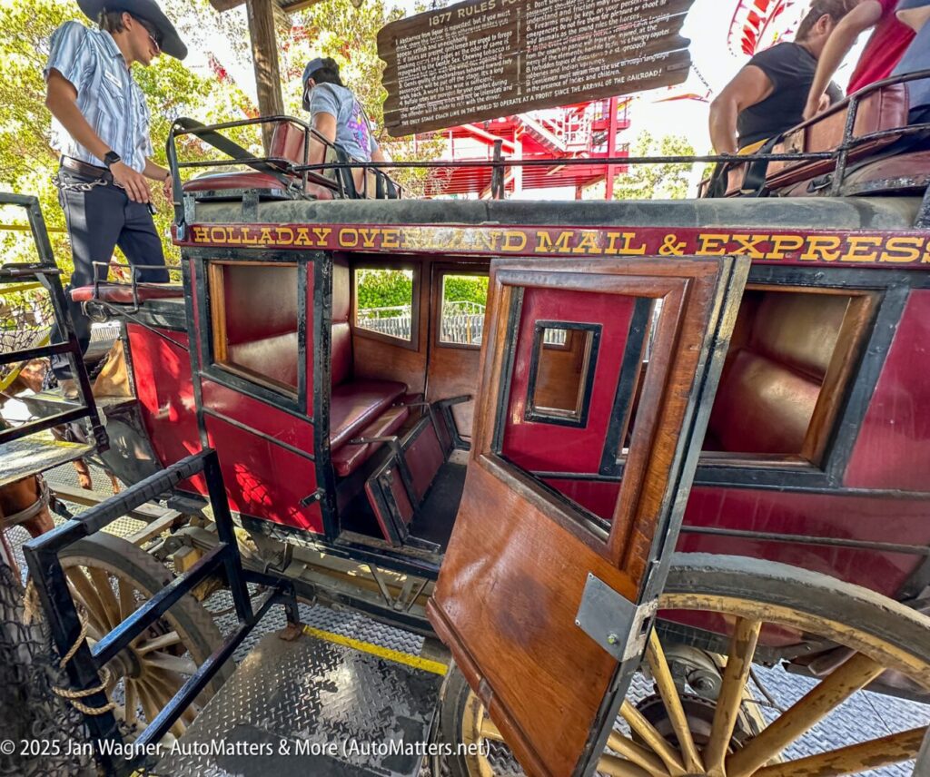 A vintage stagecoach labeled "HOLLADAY OVERLAND MAIL & EXPRESS" with open doors, showing wooden seats and steps for boarding.