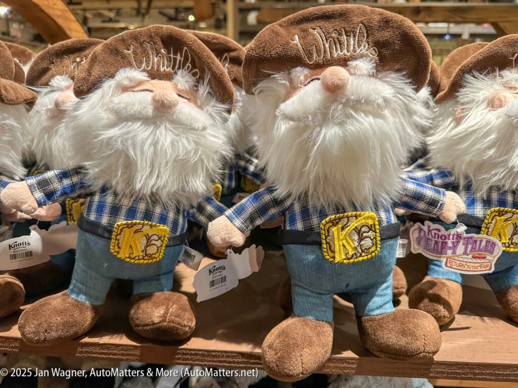 Several plush gnome dolls with white beards, plaid shirts, brown hats labeled "Whittles," and yellow "KC" belt buckles are displayed on a wooden shelf.