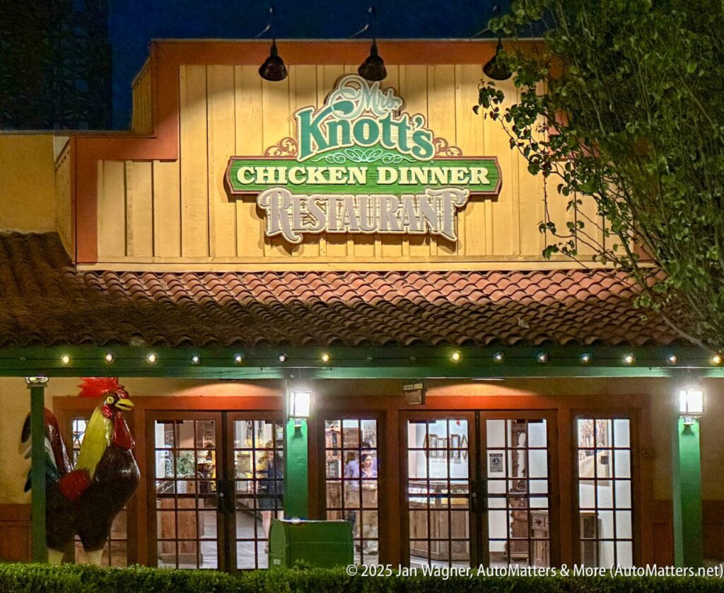 Exterior of Mrs. Knott's Chicken Dinner Restaurant at night, featuring the illuminated sign above the entrance and a large rooster statue outside.